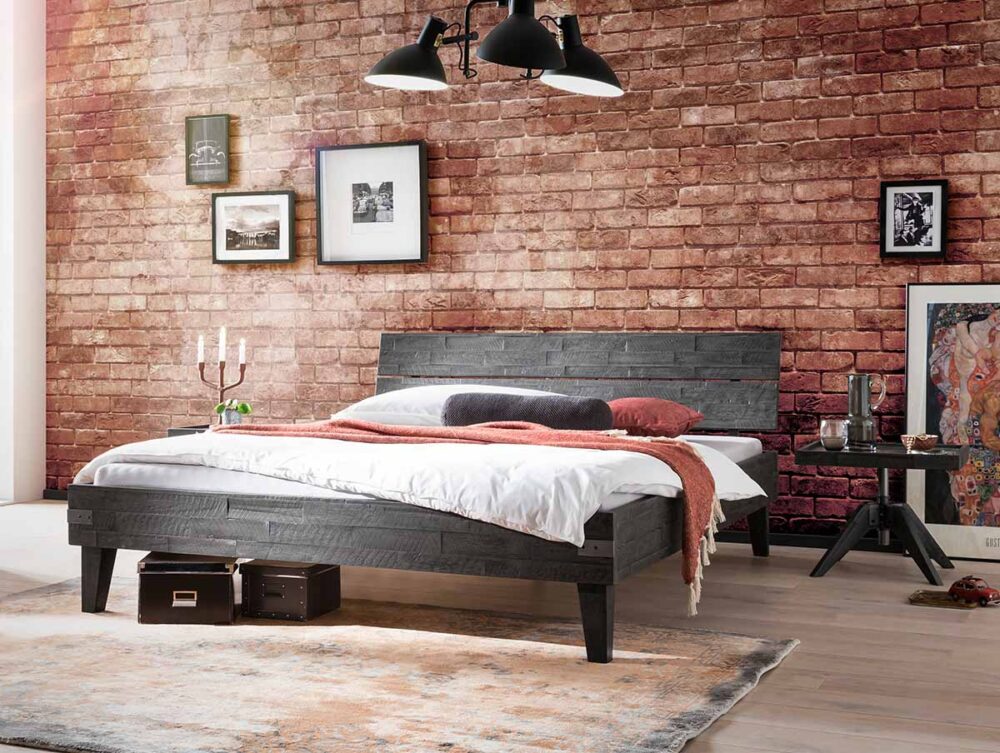 Ein modernes Schlafzimmer mit einem dunklen Holzbett, weißer Bettwäsche und einer rostfarbenen Überwurfdecke. Der Raum verfügt über eine Akzentwand aus Ziegelsteinen, gerahmte Kunstwerke, einen Teppich und Pendelleuchten im industriellen Stil.