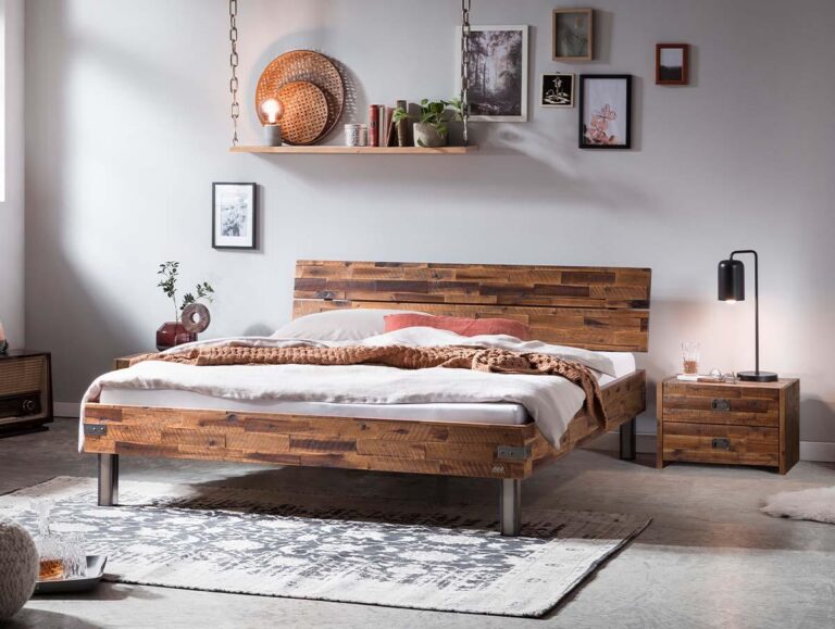 Ein gemütliches Schlafzimmer mit einem hölzernen Bettgestell, weißer Bettwäsche, einer braunen Decke, einem Nachttisch mit einer Lampe, einer Hängelampe, gerahmter Kunst an der Wand und einem gemusterten Teppich auf einem Betonboden.