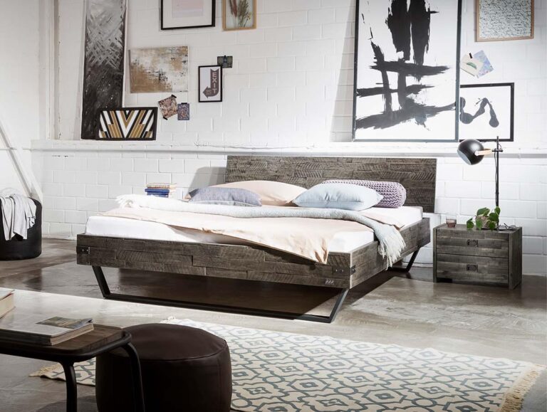 Ein modernes Schlafzimmer mit einem Holzbett, weicher rosa und weißer Bettwäsche, einem gemusterten Teppich, einem Nachttisch mit Lampe und Pflanze, Wandkunst und dekorativen Akzenten vor einer weißen Backsteinwand.
