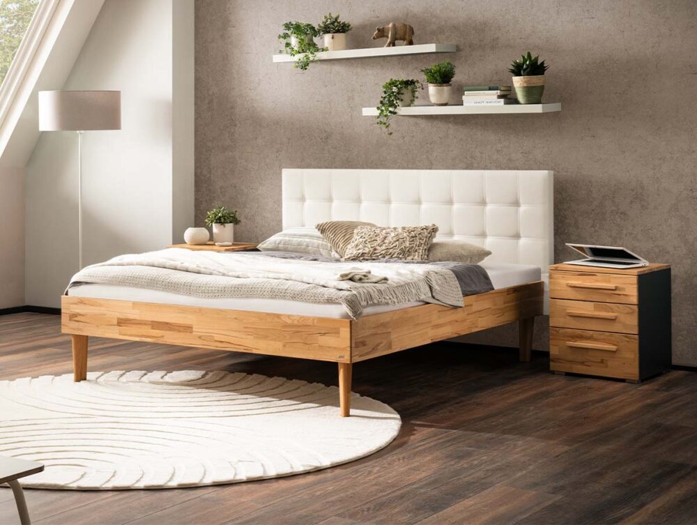 Ein modernes Schlafzimmer mit einem Holzbett, einem weißen getufteten Kopfteil, gemütlicher Bettwäsche, einem runden weißen Teppich, einem hölzernen Nachttisch, zwei Wandregalen mit Pflanzen, einer Lampe und Sonnenlicht, das durch ein großes Fenster fällt.