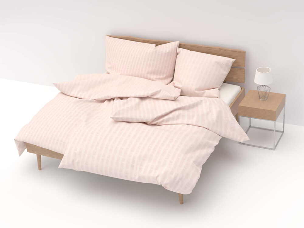 Ein Holzbett mit Bettwäsche Satin Seersucker rosa und drei Kissen steht neben einem hölzernen Nachttisch mit einer kleinen weißen Lampe, alles in einem minimalistischen, weißen Raum.