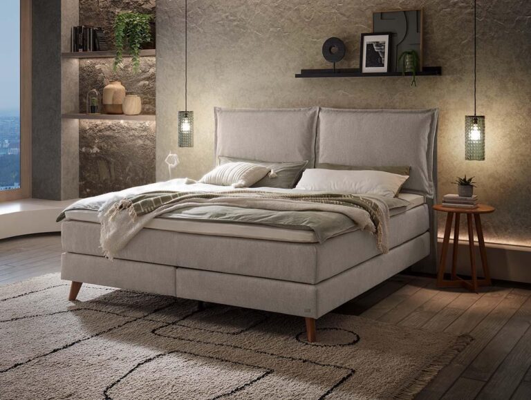 Ein modernes Schlafzimmer mit einem beigen Polsterbett, grüner und weißer Bettwäsche, einem strukturierten Teppich, hängenden Pendelleuchten, schwebenden Regalen mit Dekoration und einem Fenster mit Blick auf die Stadt.