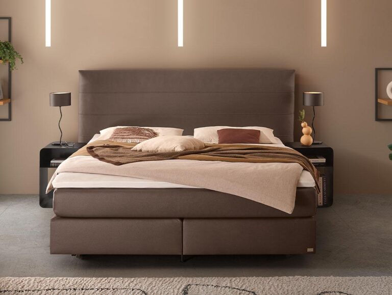 Ein modernes Schlafzimmer mit einem großen braunen Polsterbett, beiger und brauner Bettwäsche, zwei schwarzen Nachttischen mit Lampen und minimalem Wanddekor. Der Raum hat eine neutrale Farbpalette und ein modernes Design.