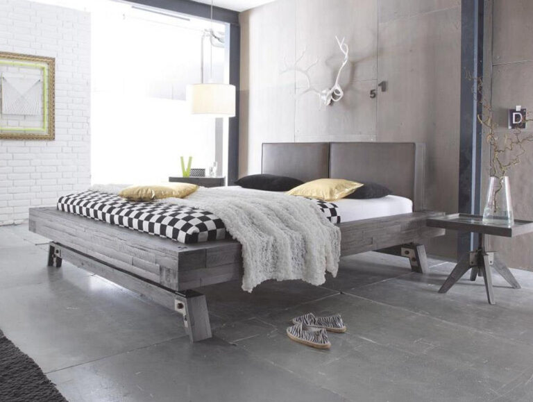 Ein modernes Schlafzimmer mit dem Holzbett "Factory-Line Bloc Stabil 1" von Hasena Bett, schwarz-weiß karierter Bettwäsche, goldenen Kissen, einer flauschigen Decke, Wanddekoration aus Geweih und einem kleinen Beistelltisch mit Vase.