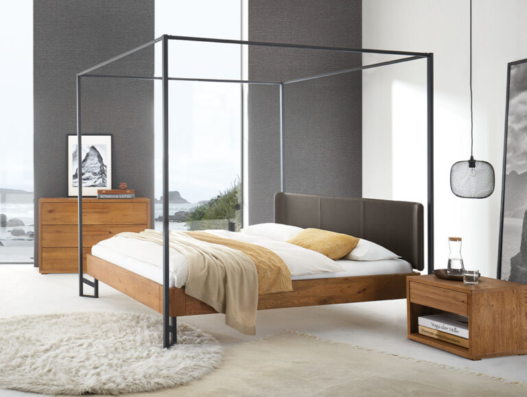 Ein modernes Schlafzimmer mit einem Himmelbett aus Holz, weißer und beiger Bettwäsche, einem runden Teppich, einem Nachttisch und einer Kommode aus Holz sowie einem großen Fenster mit Blick auf die Küste. Minimalistisches Dekor mit neutralen Tönen.