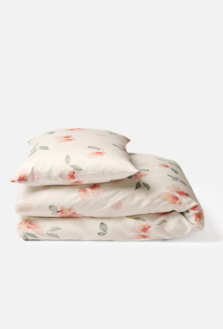 Ein gefaltetes Set aus cremefarbener Bettwäsche mit einem Blumenmuster aus rosa Blüten und grünen Blättern, einschließlich eines Kissenbezugs, der auf einem Bettbezug liegt.