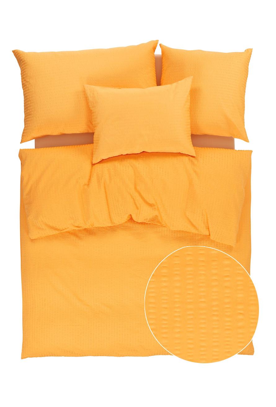 Ein ordentlich gemachtes Bett mit einem orangefarbenen strukturierten Bettbezug und drei passenden Kissen; ein kreisförmiger Einsatz zeigt eine Nahaufnahme des detaillierten Musters des Stoffes.