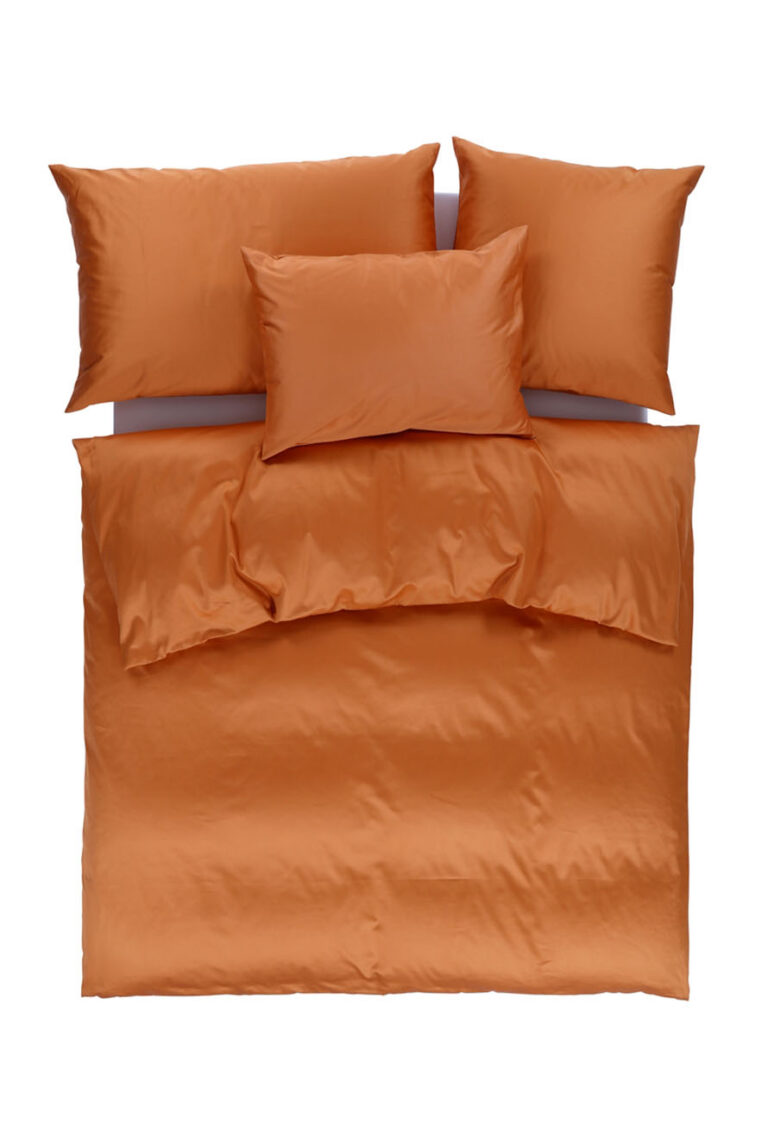 Ein ordentlich gemachtes Bett mit einem orangefarbenen Bettbezug, zwei großen orangefarbenen Kissen und zwei mittelgroßen orangefarbenen Kissen auf einem weißen Hintergrund.