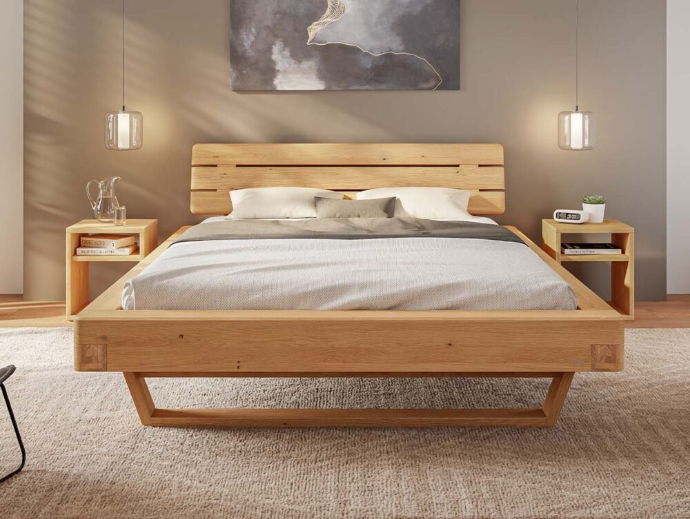 Ein modernes Holzbett mit einem hellen Holzrahmen, zwei passenden Nachttischen, hängenden Pendelleuchten und neutraler Bettwäsche in einem minimalistisch eingerichteten Schlafzimmer. Über dem Bett hängt ein großes abstraktes Gemälde.