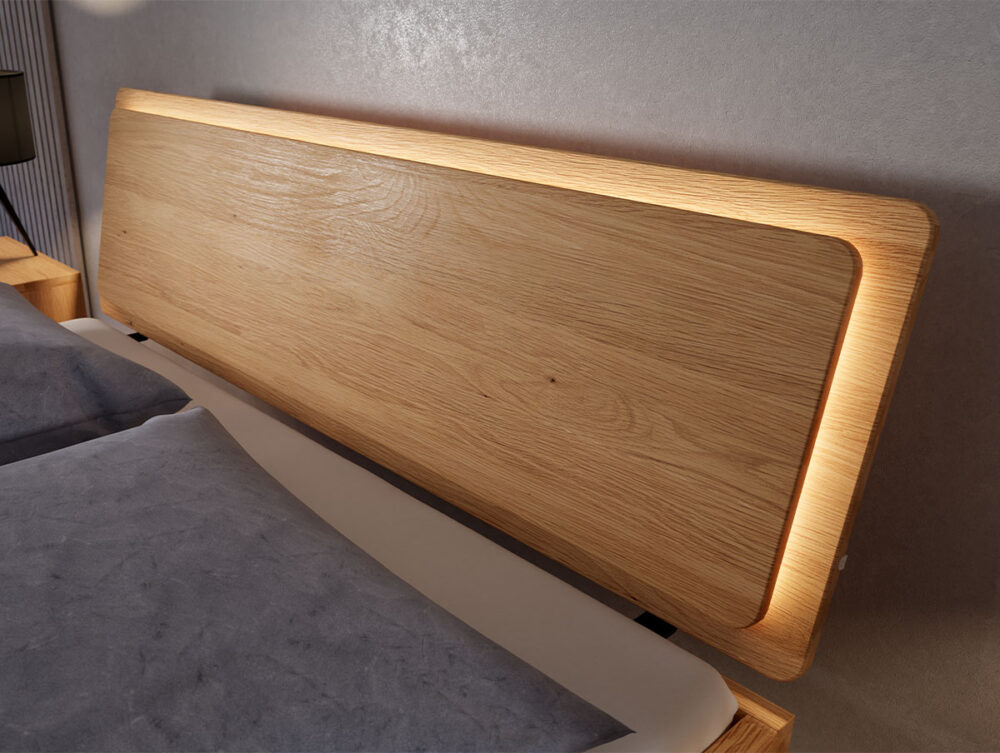 Ein modernes Bettkopfteil aus Holz mit einer glatten, hellen Holzoberfläche und integrierter Stimmungsbeleuchtung, das an einer hellen Wand neben einem ordentlich gemachten Bett in neutralen Farbtönen steht.