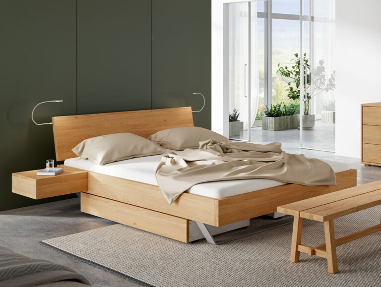 Modernes Schlafzimmer mit einem Holzbett, beiger Bettwäsche, hängenden Nachttischen und minimalistischen Lampen. Große Fenster lassen Tageslicht herein und geben den Blick auf die Topfpflanzen draußen frei. Eine Holzbank und eine Kommode runden die Einrichtung ab.