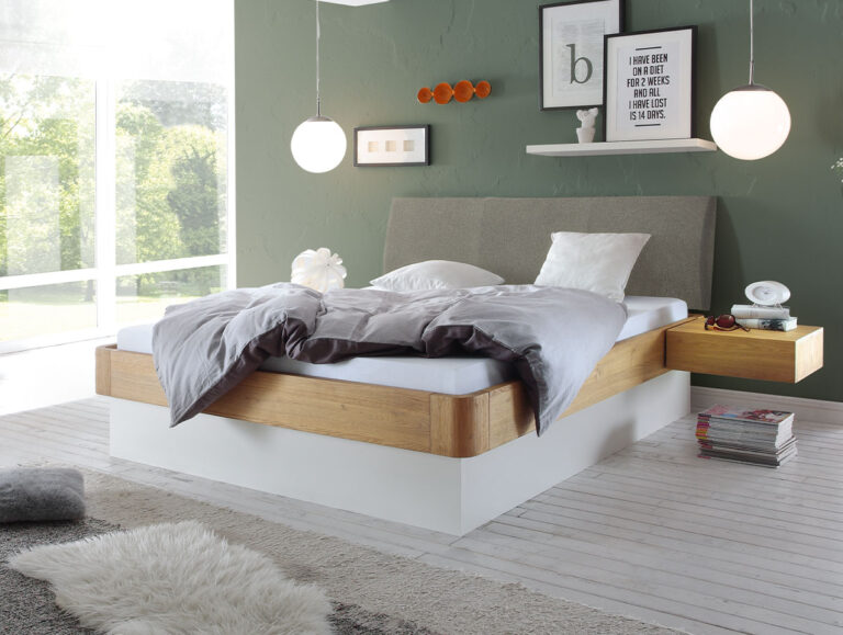 Modernes Schlafzimmer mit einem freischwebenden Holzbett, grauer Bettwäsche, einer grünen Akzentwand, runden Hängelampen, Wandkunst und einem freischwebenden Nachttisch mit Büchern. Große Fenster lassen Tageslicht herein.