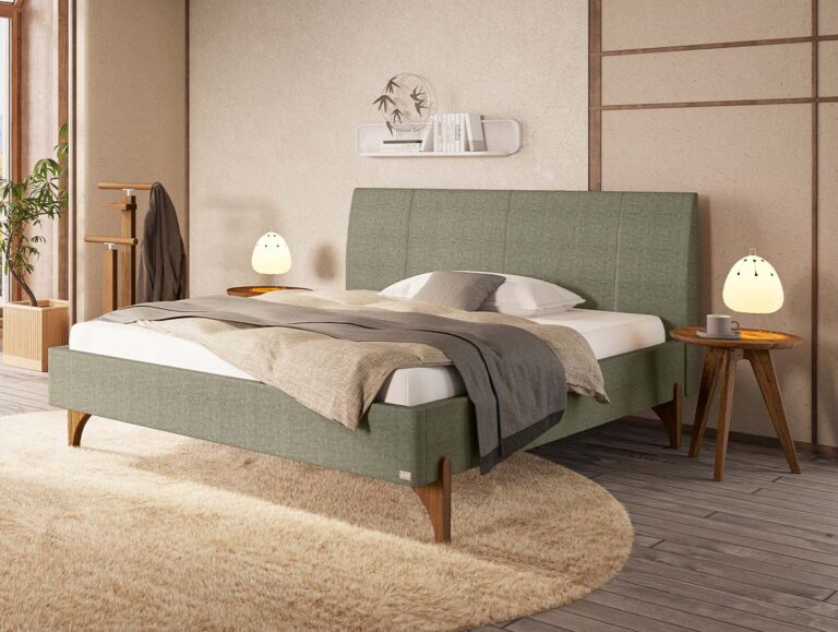 Modernes Schlafzimmer mit einem grün gepolsterten Bett, grauer und beiger Bettwäsche, runden Beistelltischen aus Holz, leuchtenden Lampen, einem beigen Teppich und minimalistischer Einrichtung vor einer neutralen Wand.