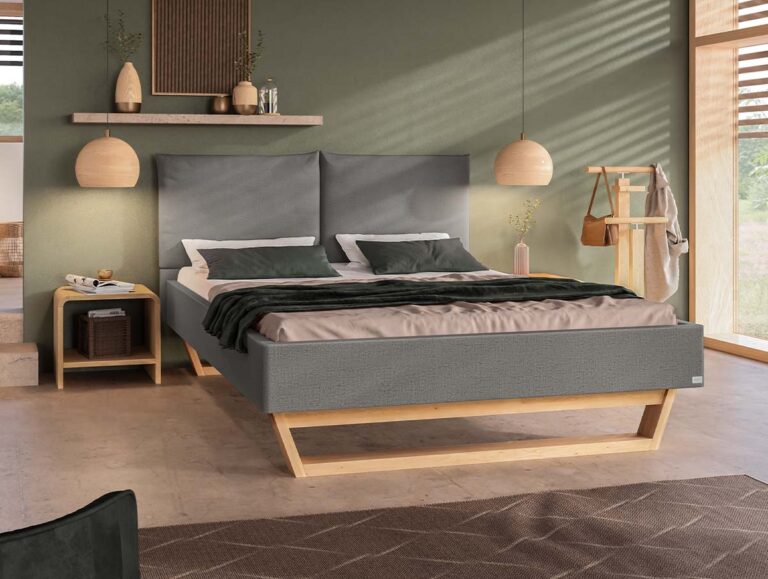 Ein modernes Schlafzimmer mit einem grauen Polsterbett, grüner Bettwäsche, Nachttischen aus Holz, hängenden Pendelleuchten und einem Kleiderständer. Große Fenster lassen Tageslicht herein, und die Einrichtung ist minimalistisch.