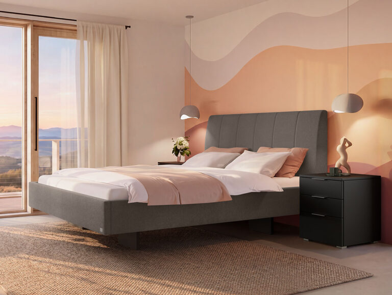 Modernes Schlafzimmer mit einem grauen Polsterbett, Bettwäsche in Blush-Farbtönen, einem schwarzen Nachttisch, einer skulpturalen Lampe und einer Vase mit Blumen. Ein großes Fenster mit transparenten Vorhängen bietet einen malerischen Blick ins Freie. An der Wand befindet sich ein wellenförmiges Wandbild in Pastelltönen.