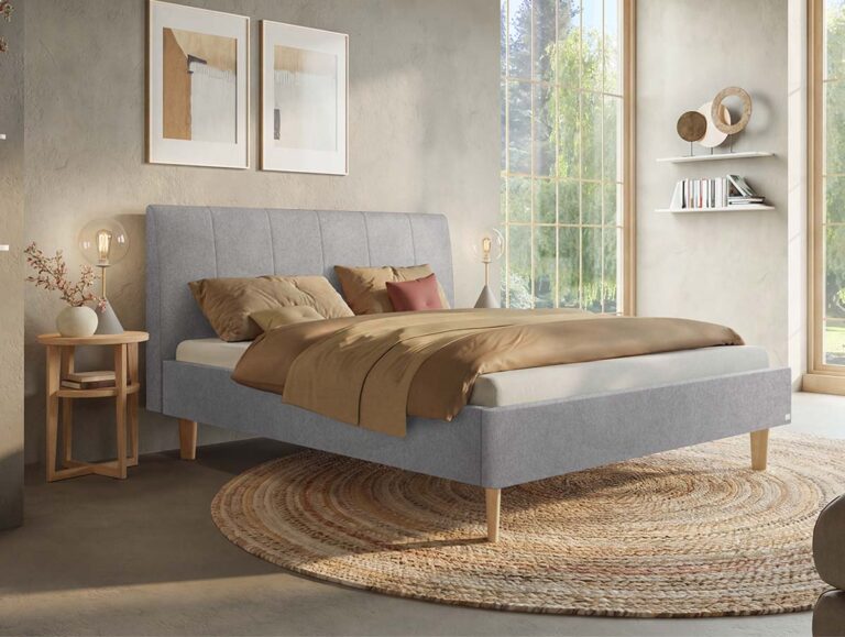 Modernes Schlafzimmer mit einem grauen Polsterbett, hellbrauner Bettwäsche, einem runden gewebten Teppich, einem Nachttisch aus Holz, abstrakter Wandkunst, großen Fenstern und sanftem Tageslicht.