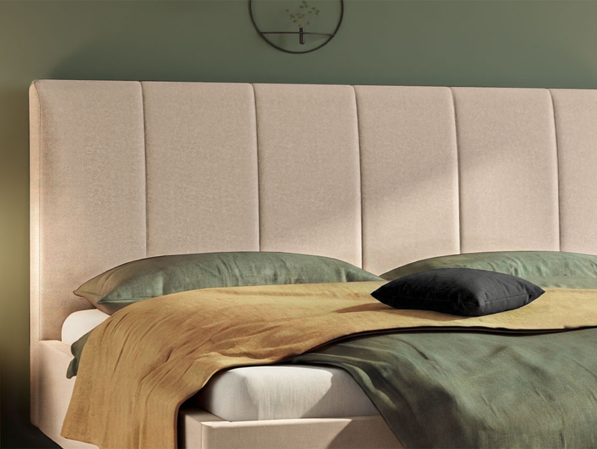 Ein modernes Bett mit einem hohen, beigen, gepolsterten Kopfteil, grüner und goldfarbener Bettwäsche und einem kleinen schwarzen Kissen. Die Wand hinter dem Bett ist grün, und darüber hängt eine runde, schlichte Uhr.