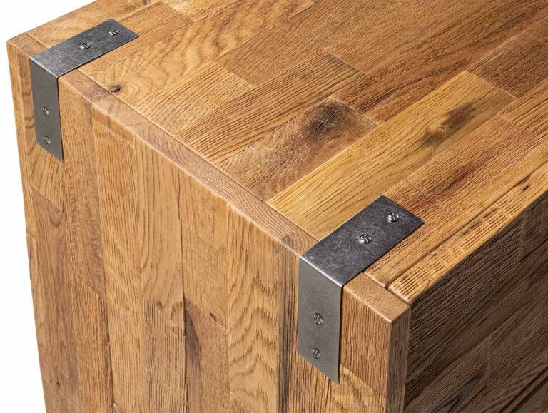 Ecke eines Möbelstücks aus Holz mit an den Oberkanten verschraubten L-förmigen Metallhalterungen.