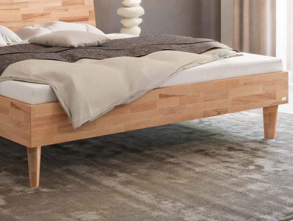 Ein helles Holzbettgestell mit einer Matratze, Kissen und einer grauen Decke.