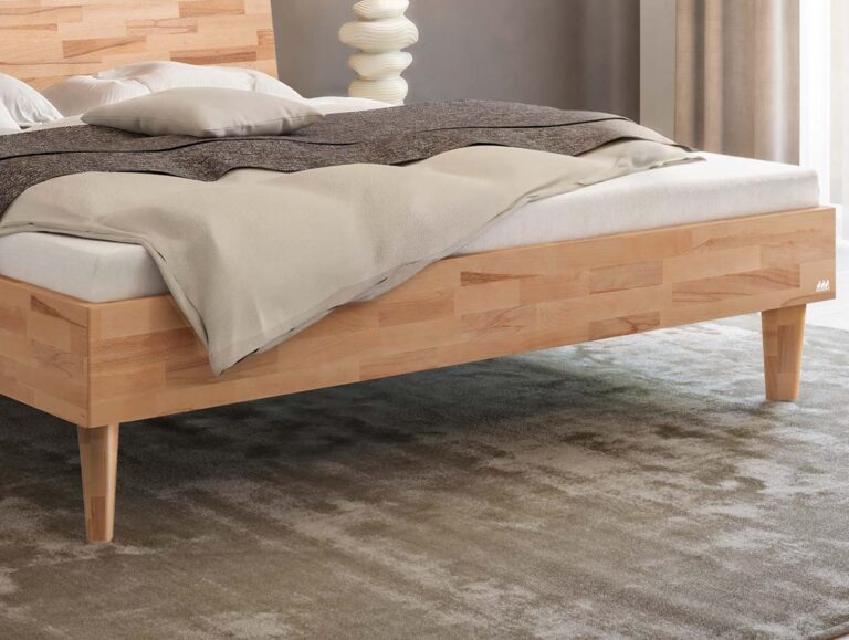 Ein helles Holzbettgestell mit einer Matratze, Kissen und einer grauen Decke.