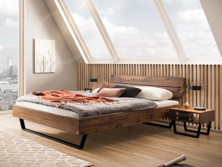 Modernes Holzbettgestell mit schwarzen Metallbeinen, das vor einer Wand aus Holzlatten unter einem schrägen Dachfenster steht.