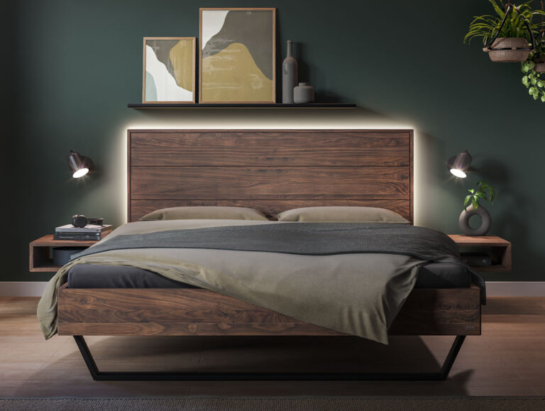 Ein Bett aus dunklem Holz mit einer hinterleuchteten Kopflehne, flankiert von an der Wand befestigten Nachttischen mit Lampen, vor einer dunkelgrünen Wand.