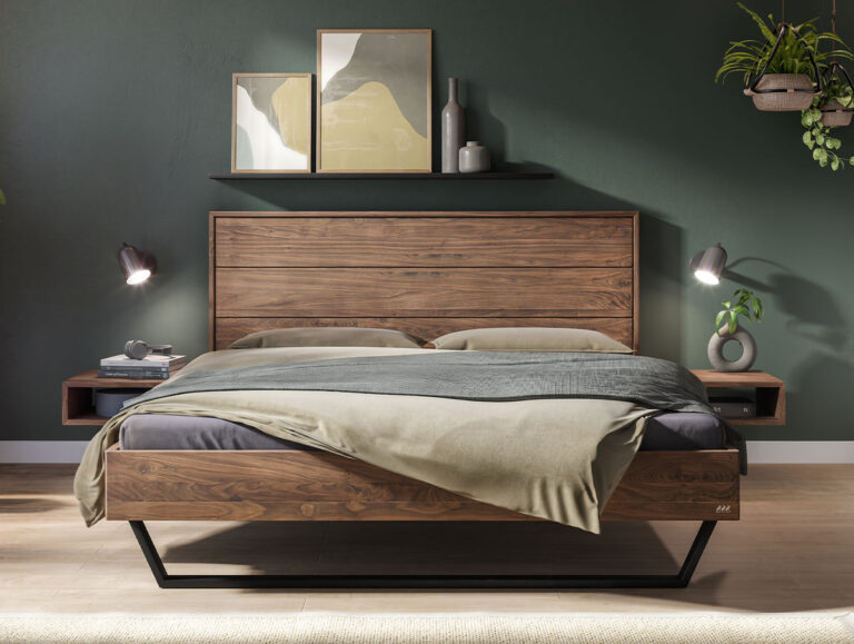 Ein Plattformbett aus Holz mit passendem Kopfteil, zwei freistehenden Nachttischen und zwei an der Wand montierten Leselampen vor einer dunkelgrünen Wand.