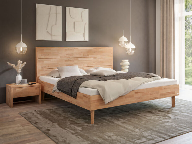 Ein helles Holzbettgestell mit Kopfteil, bezogen mit einer weißen Bettdecke, einer beigen Tagesdecke und Kissen, das auf einem grauen Teppich steht.
